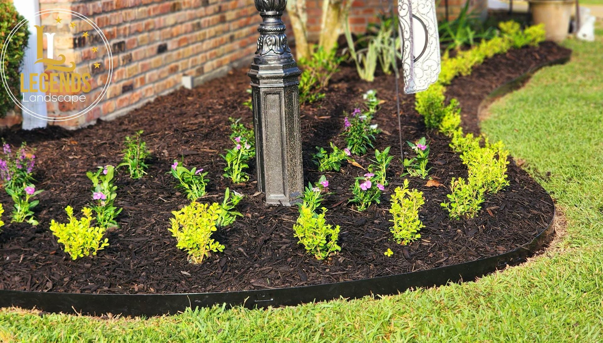 A garden with flowers and mulch in front of a brick building.