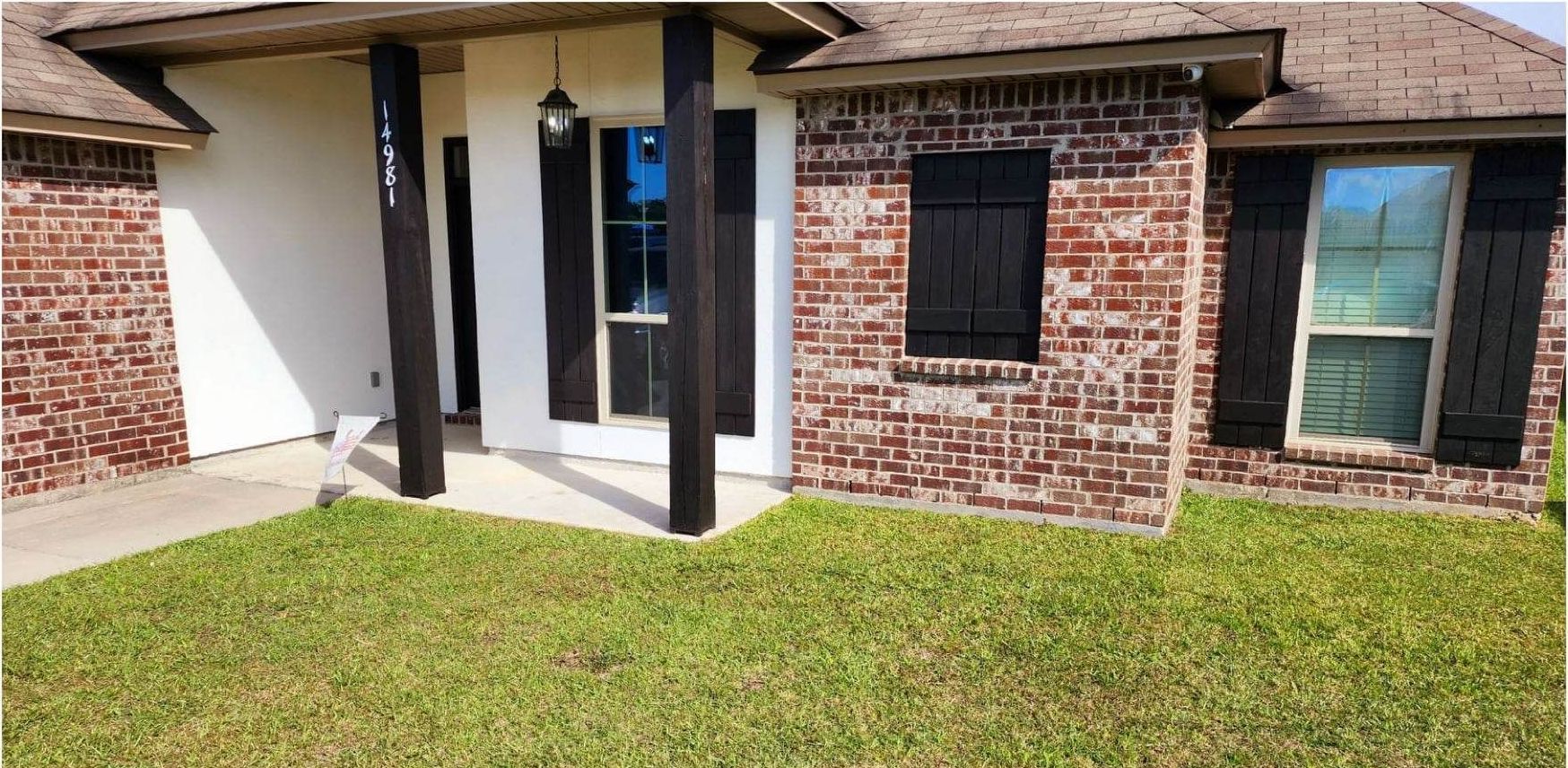 A brick house with black shutters and a large lawn in front of it.