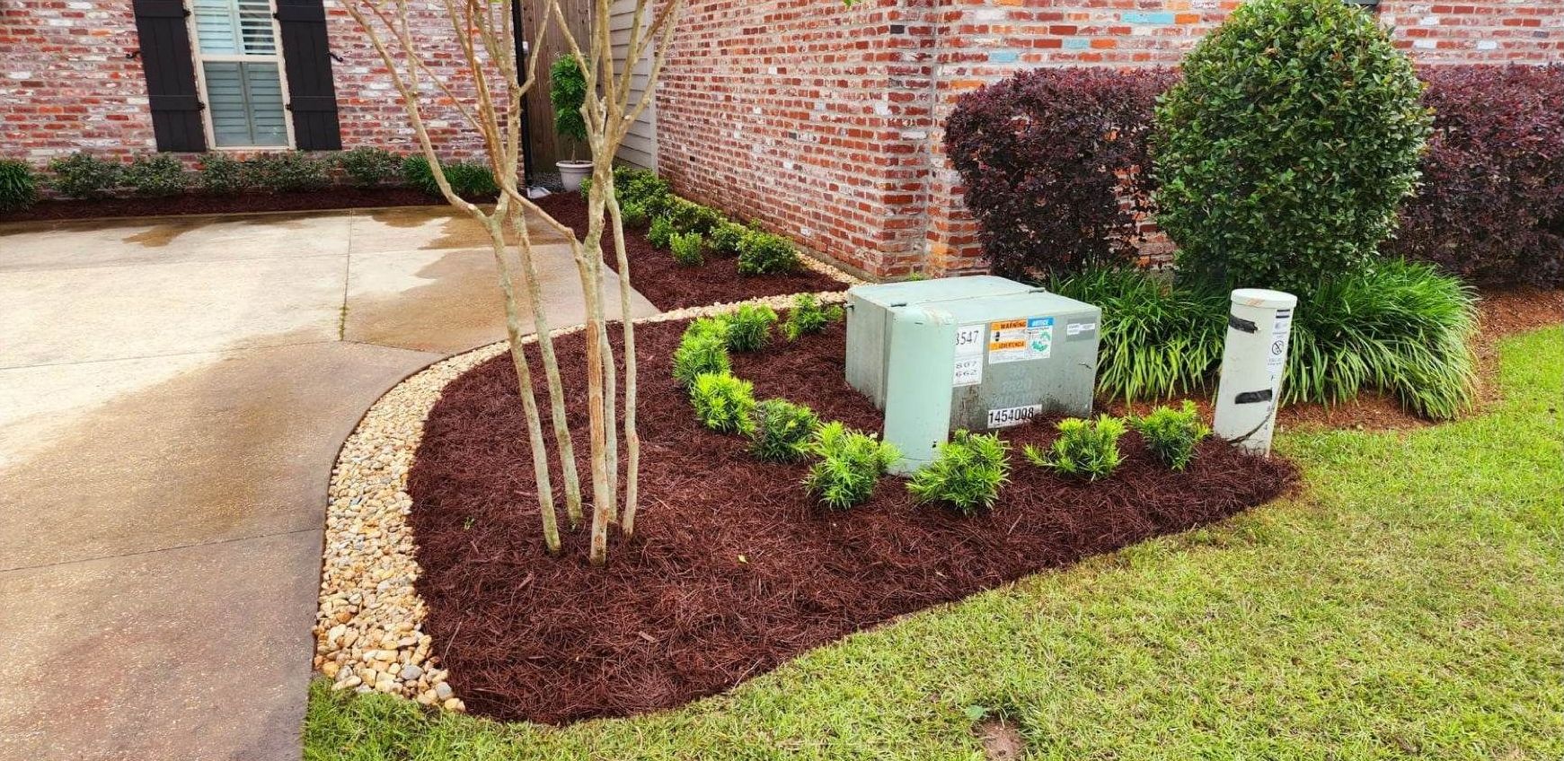 A brick house with a lush green lawn and a mulch bed in front of it.