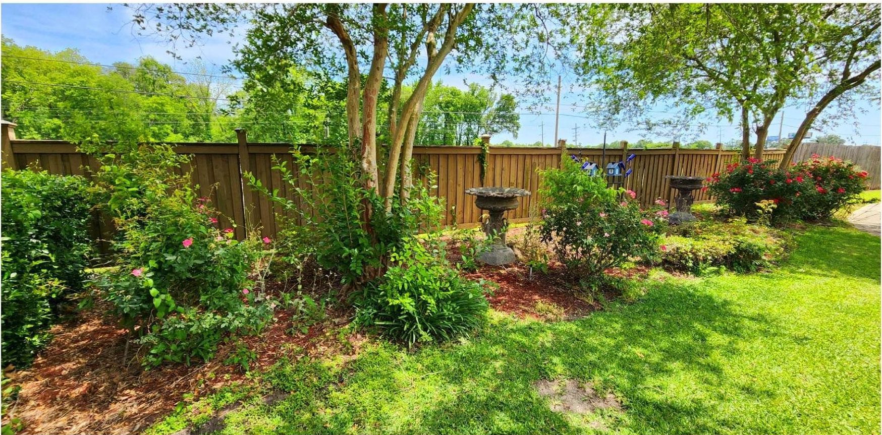 A wooden fence surrounds a lush green yard with trees and bushes.