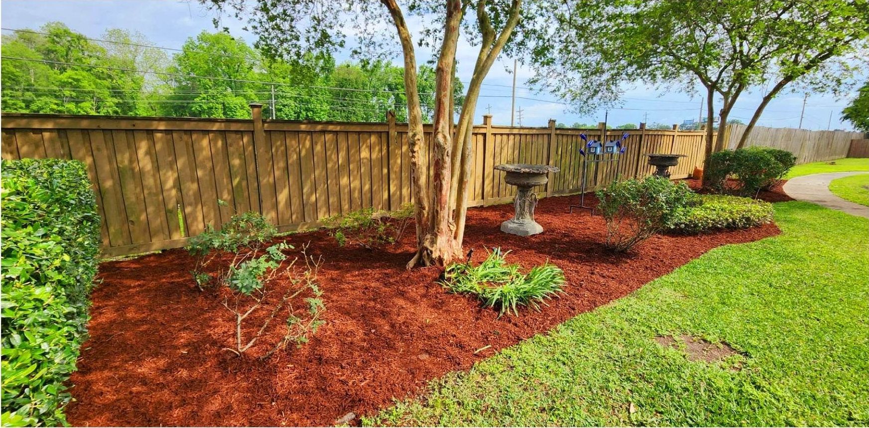 A wooden fence is surrounded by mulch and trees in a yard.