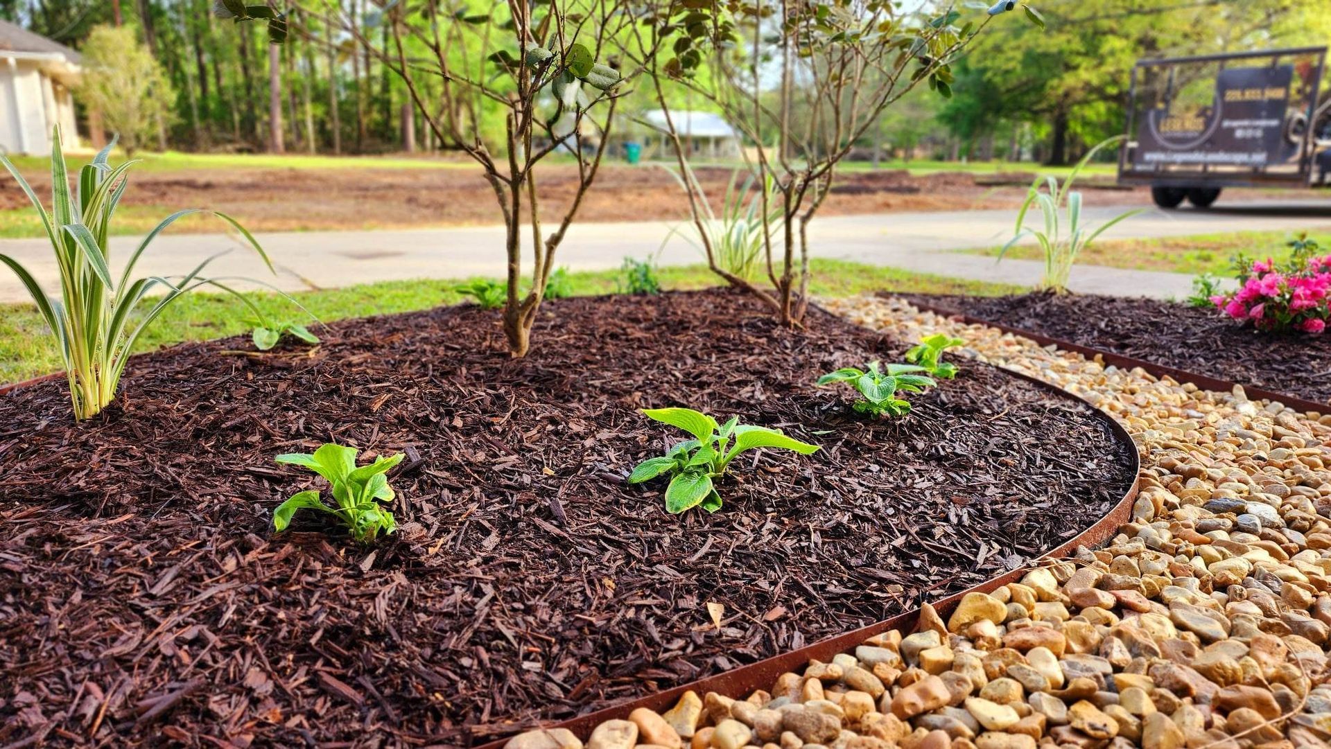 A garden filled with mulch and rocks with a truck parked in the background.