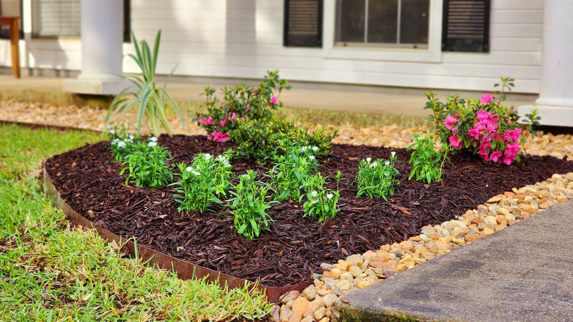 A garden with flowers and mulch in front of a house.