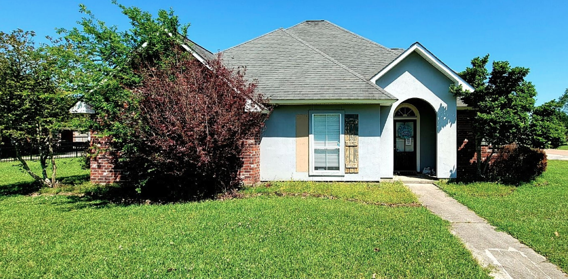A small white house with a gray roof is sitting on top of a lush green lawn.