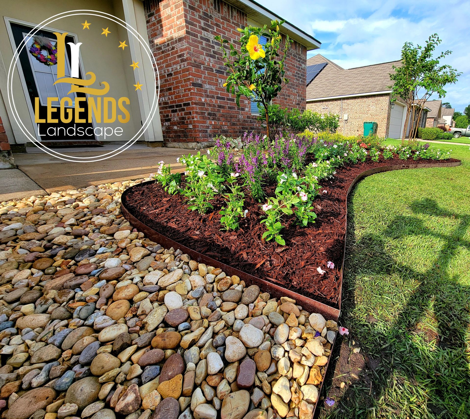 A garden with rocks and flowers in front of a brick house.