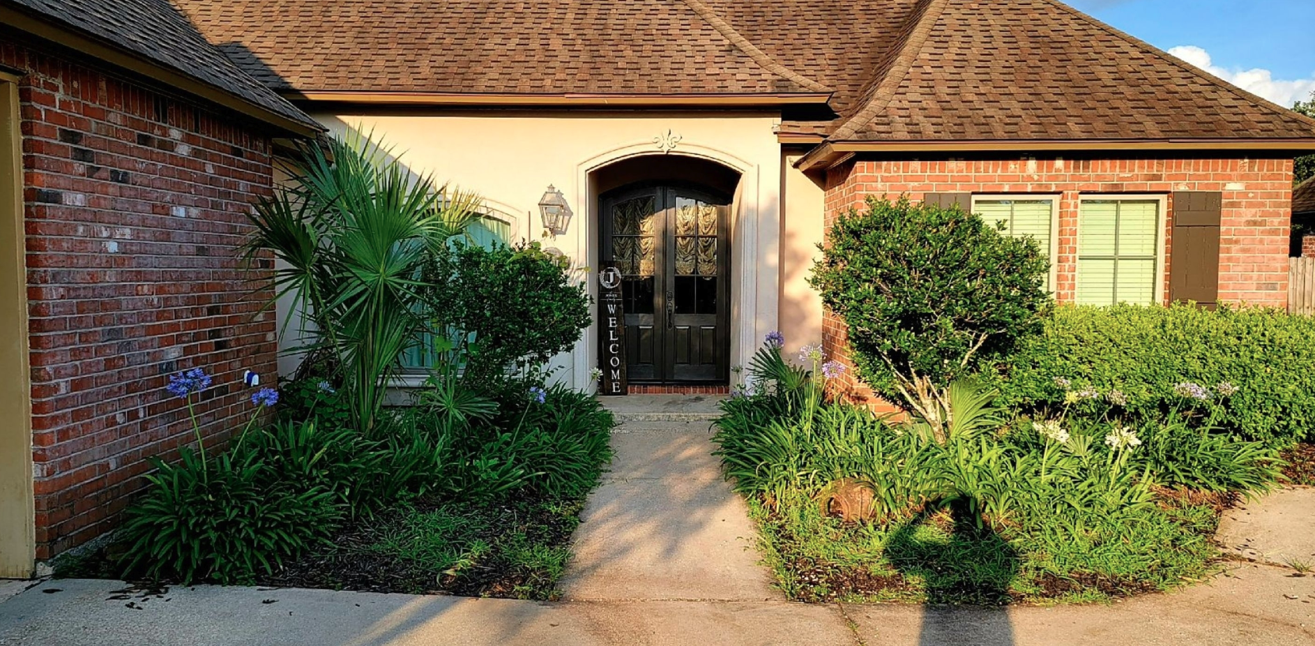 A brick house with a walkway leading to the front door surrounded by bushes and trees.