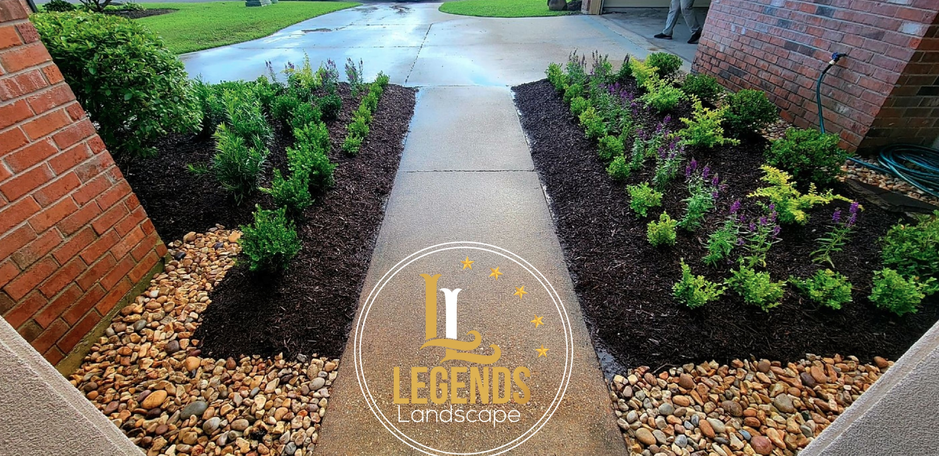 A walkway leading to a house with a brick wall and bushes along the side.