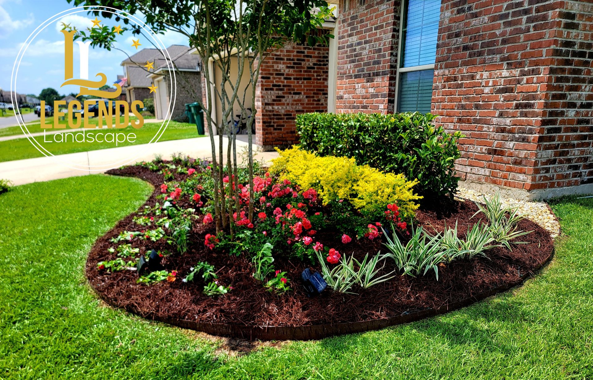 A garden with flowers and mulch in front of a brick house.