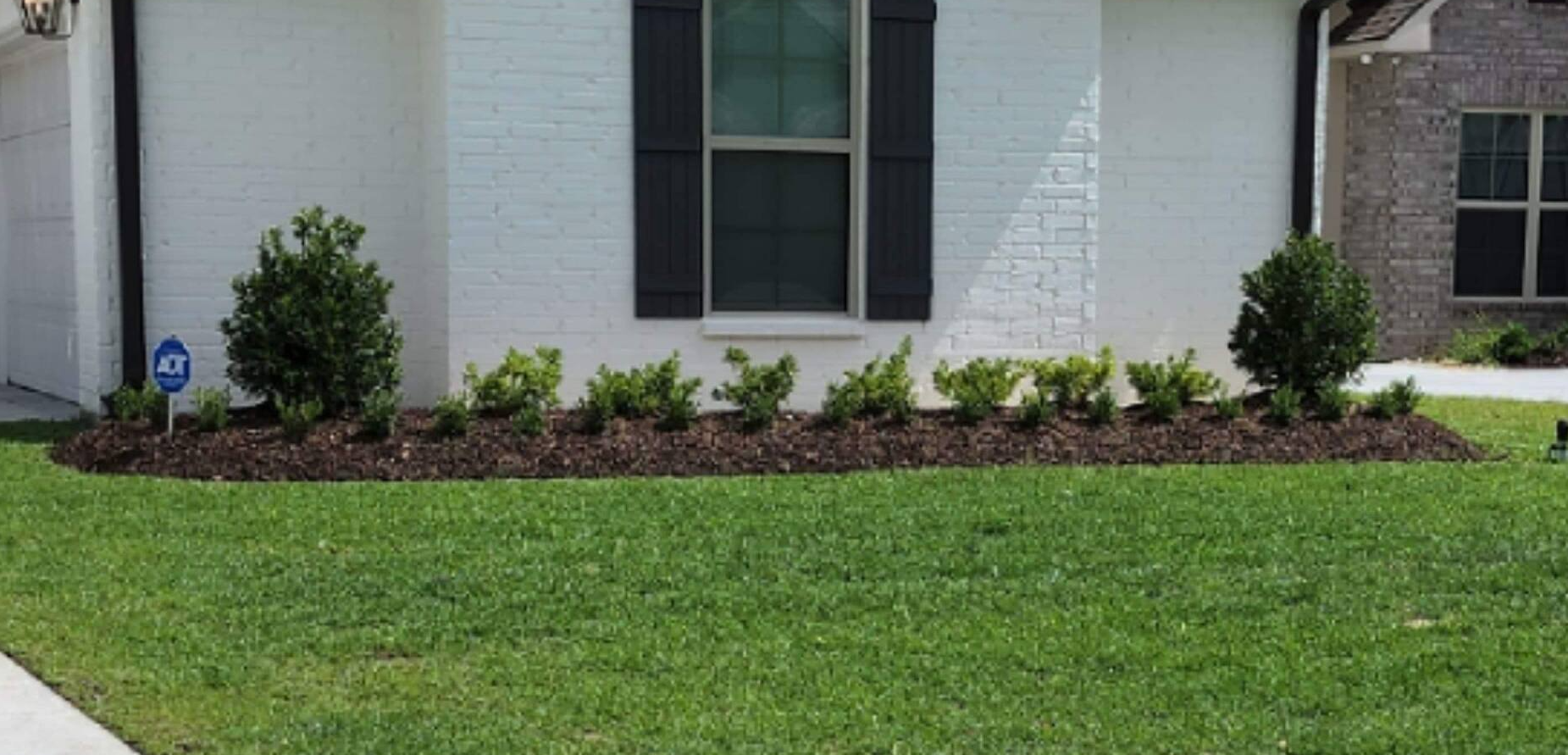 A white house with black shutters and a lush green lawn in front of it.