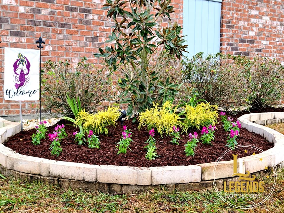A garden with flowers and a sign in front of a brick building.