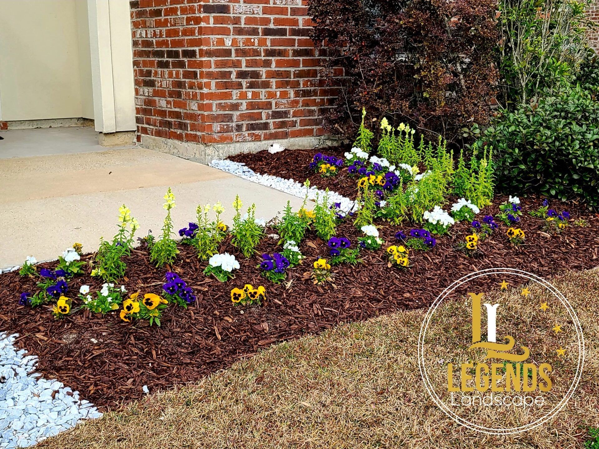A garden with flowers and mulch in front of a brick house