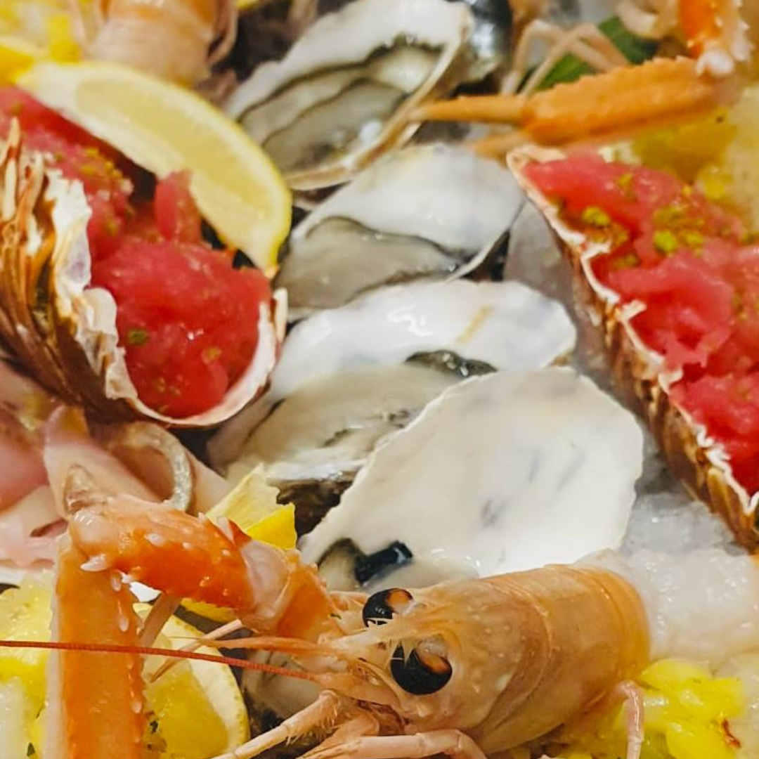 Plateau de fruits de mer : homard, crevettes, huîtres et thon servis avec des tranches de citron.