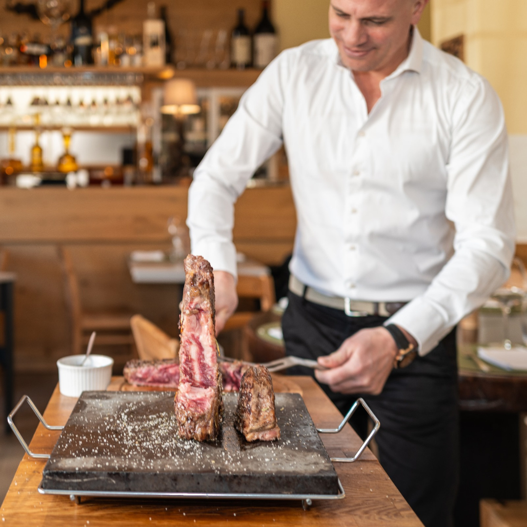 Un homme en chemise blanche découpe un steak sur une pierre chaude dans un restaurant.
