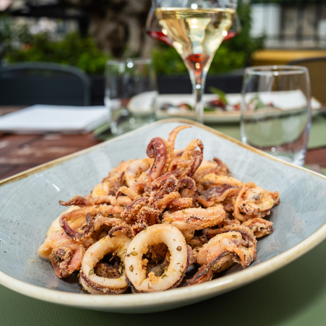 Calamars frits sur une assiette bleue, avec des verres de vin et d'eau en arrière-plan sur une table de restaurant.