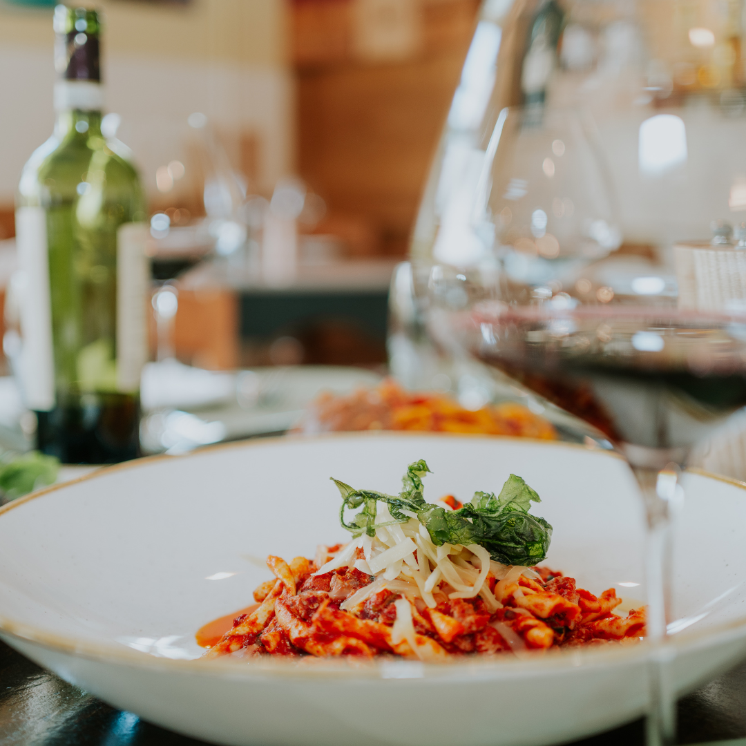 Plat de pâtes à la sauce tomate, verre de vin et bouteille sur la table.