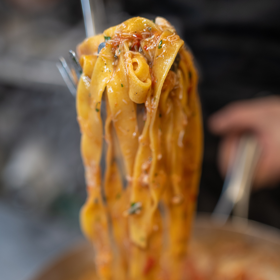 Une bouchée de pappardelles orange à la sauce tomate, prélevée de la poêle.
