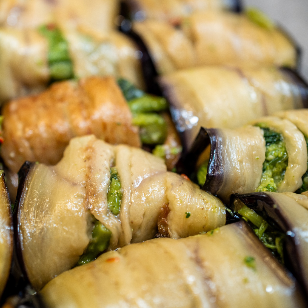 Rouleaux d'aubergine farcis d'une farce verte. Des couleurs brunes et violettes sont présentes.