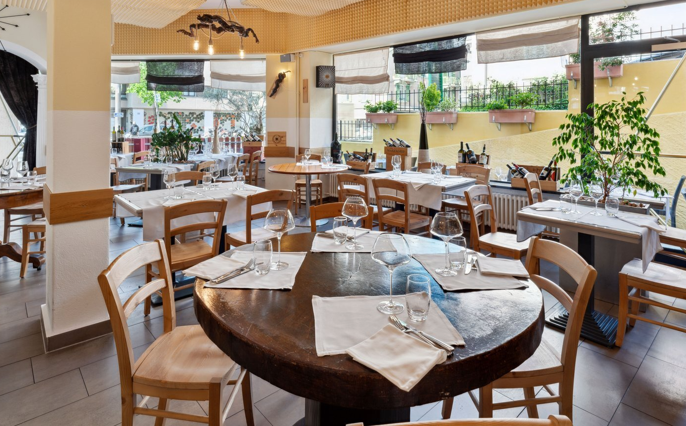 Intérieur de restaurant avec tables dressées, lumière naturelle et chaises en bois.