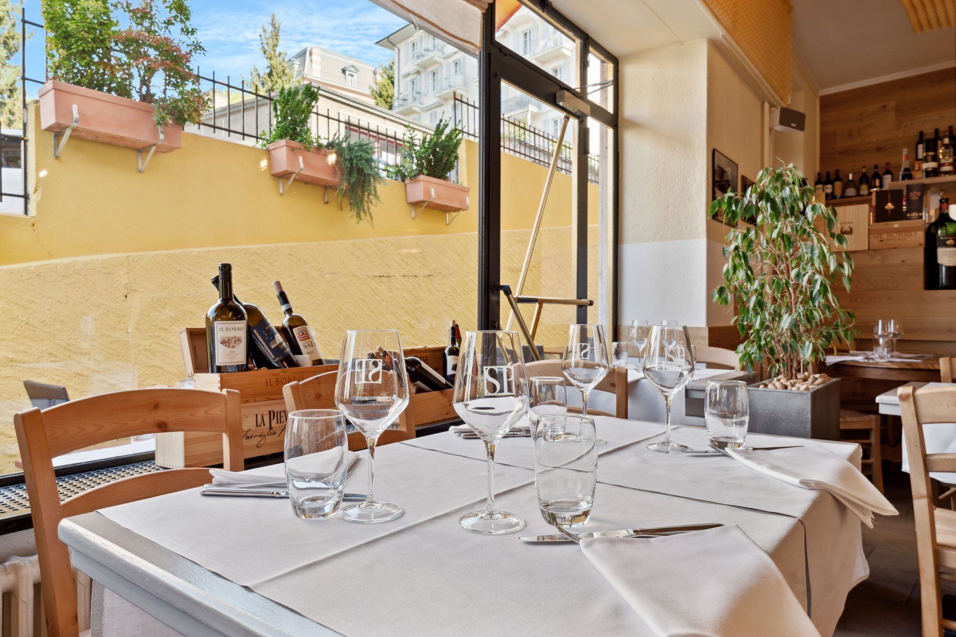Table de restaurant dressée pour le dîner, avec vue sur une terrasse extérieure, bouteilles de vin exposées.