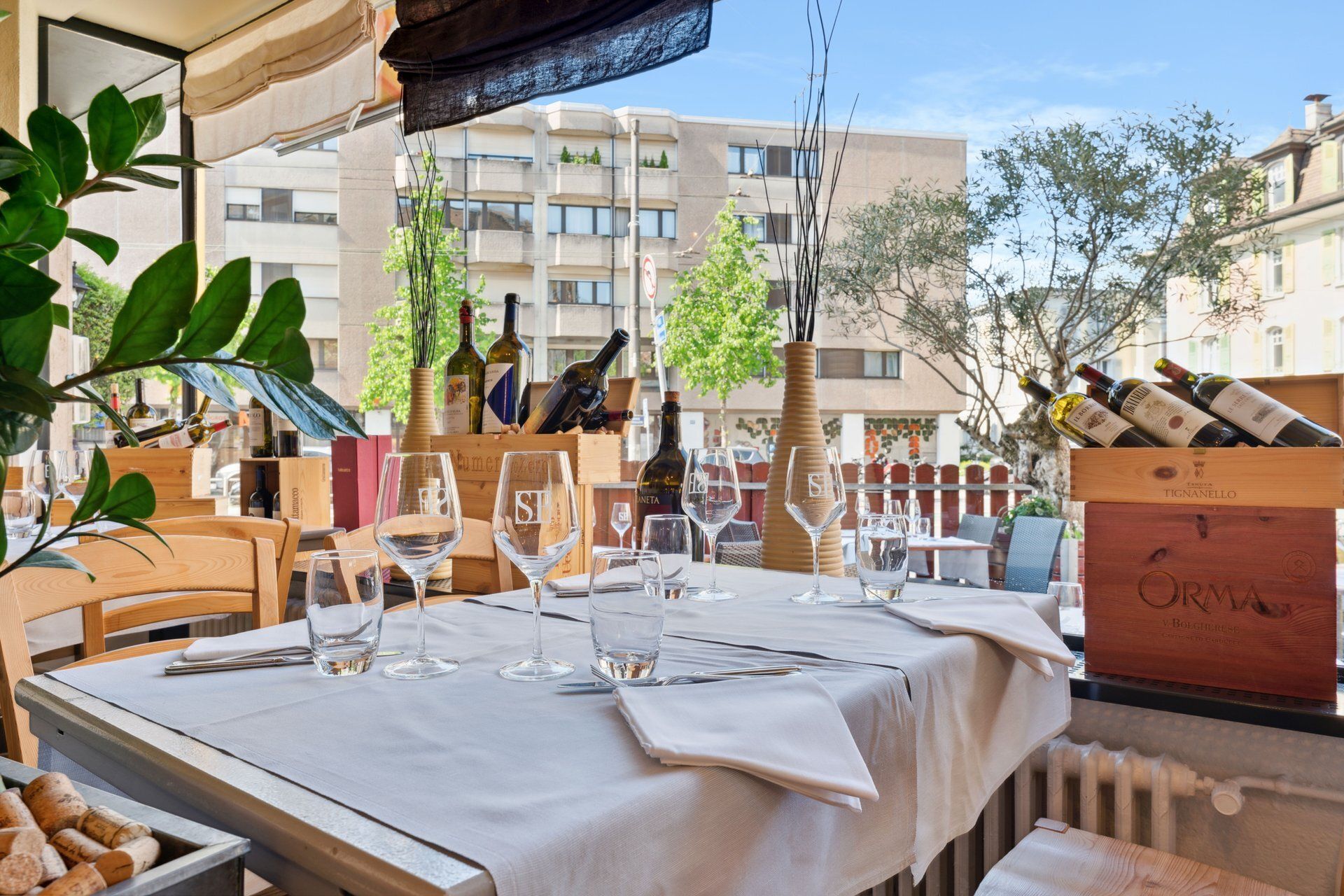 Table de restaurant dressée pour le dîner, avec bouteilles de vin et vue sur la ville.