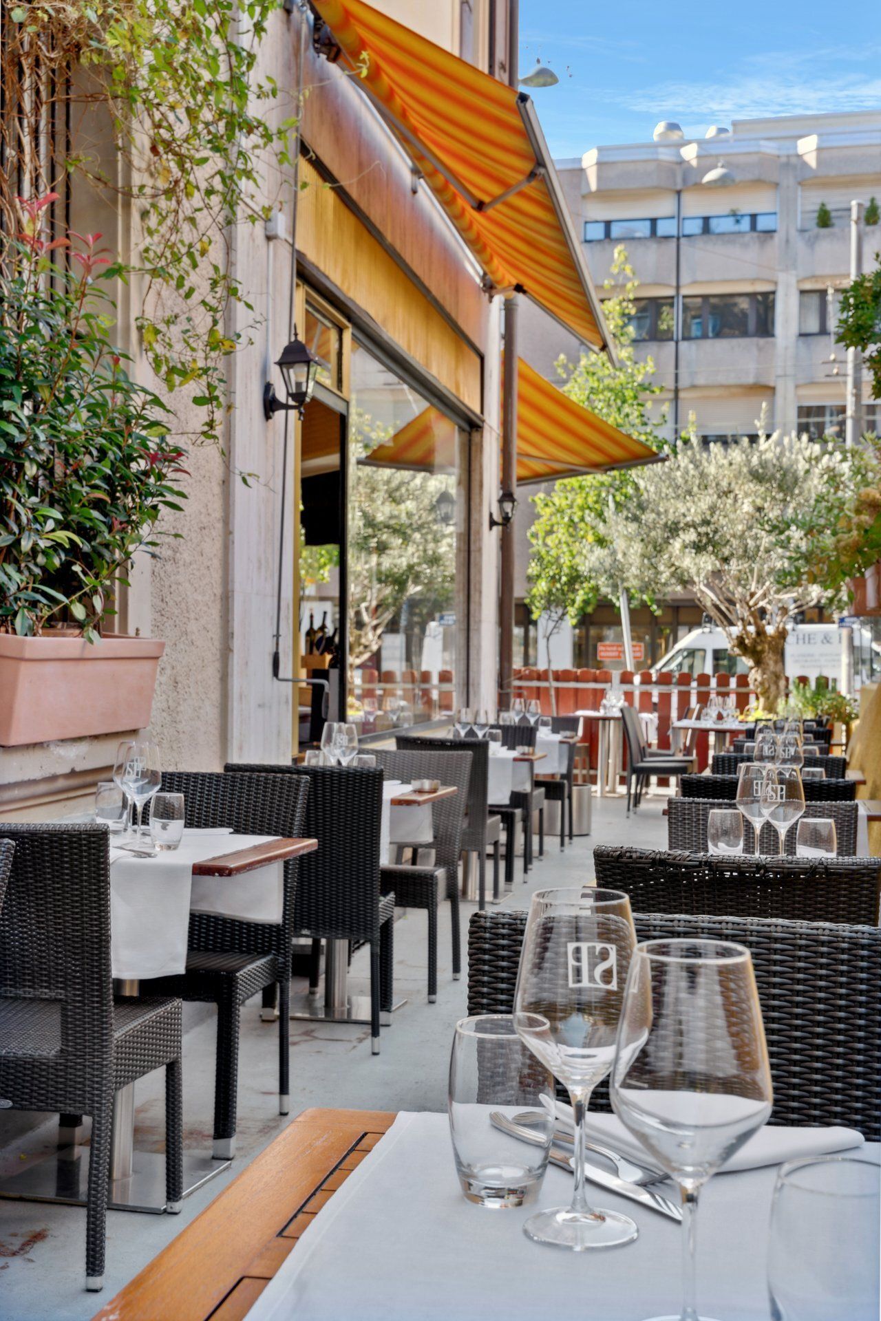 Terrasse de restaurant avec tables dressées pour dîner, sous un auvent jaune.