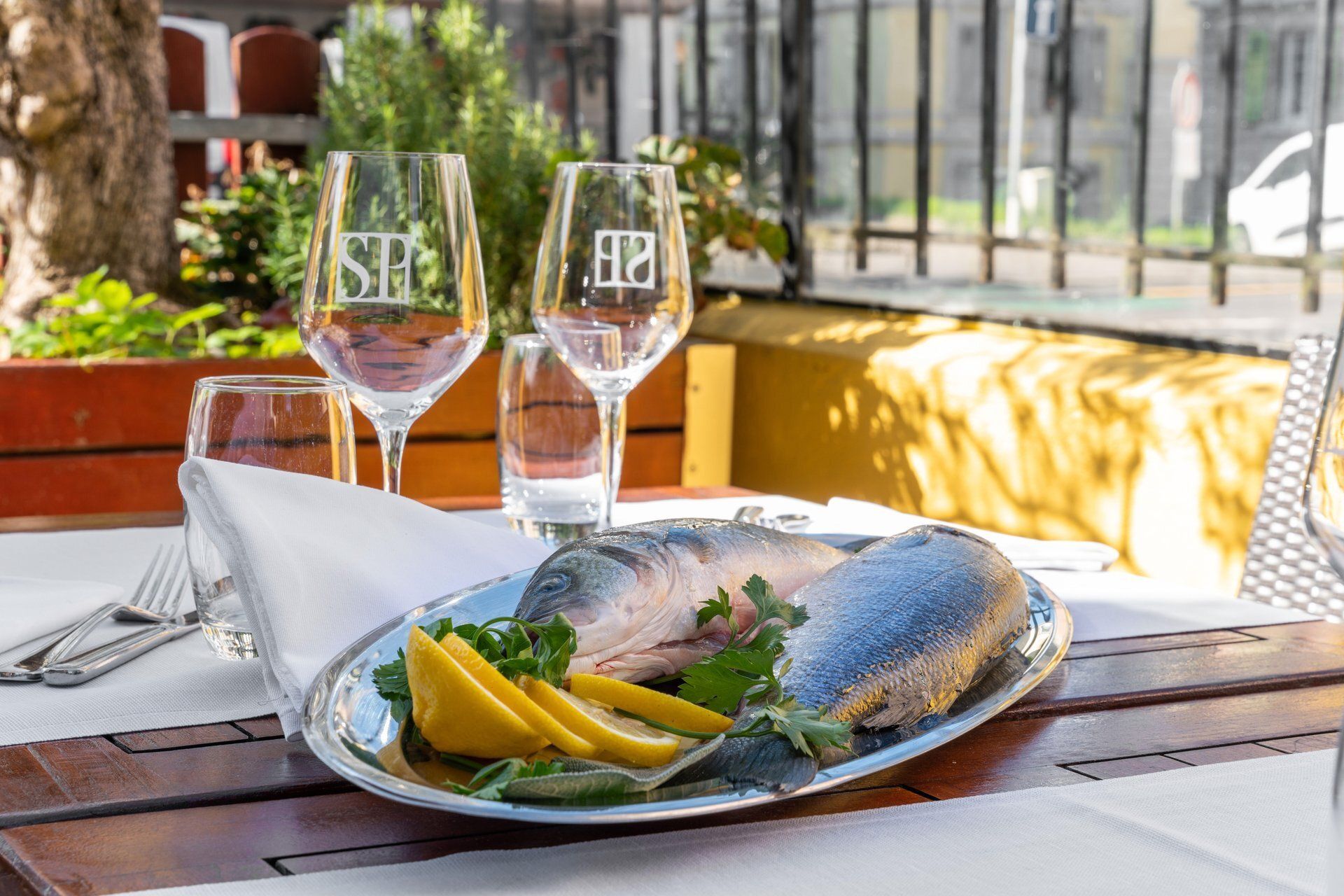 Plat de poisson avec des tranches de citron et du persil, présenté sur une table dressée avec des verres à vin.