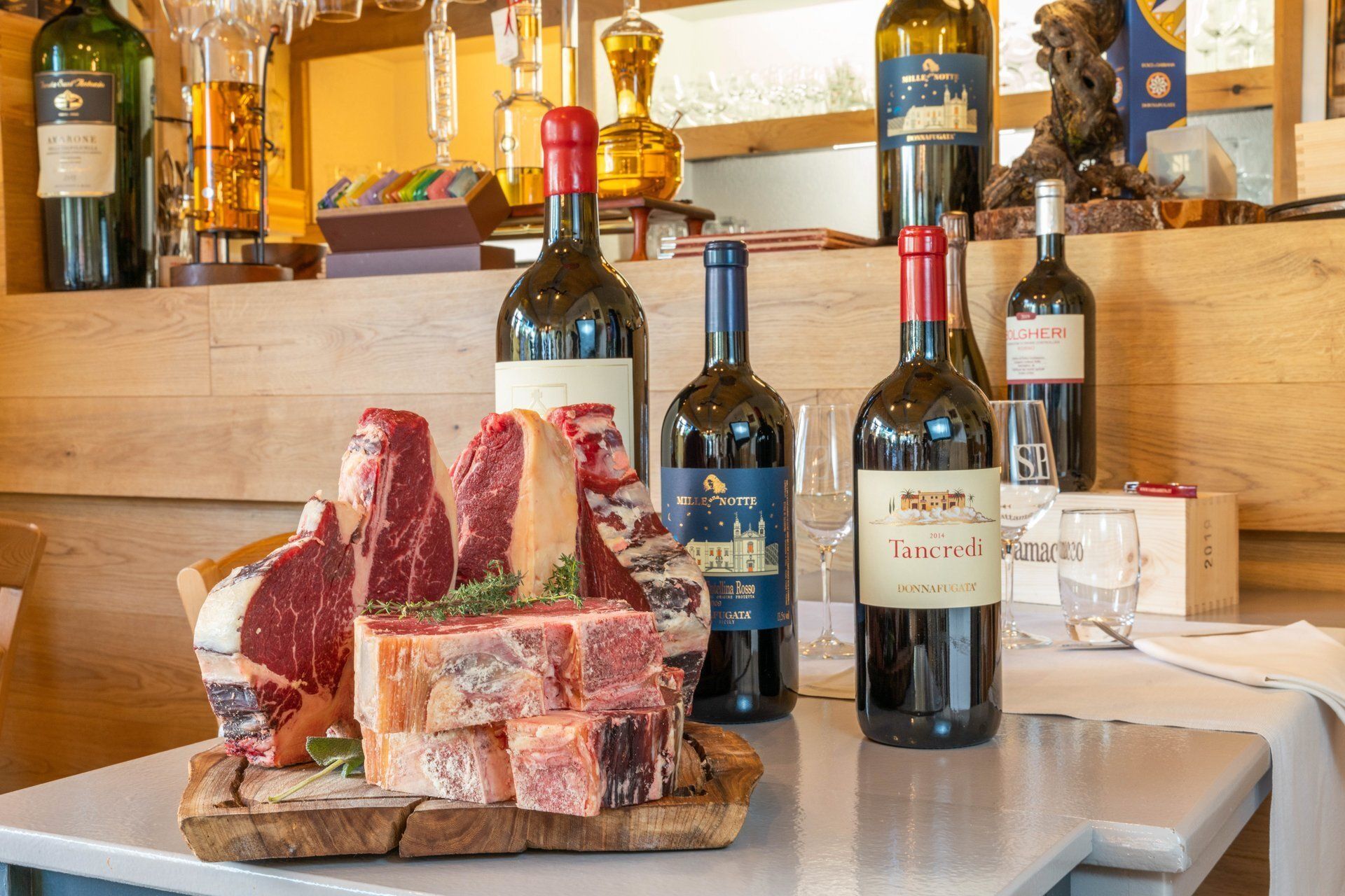 Des steaks sur une planche en bois, entourés de bouteilles de vin rouge, dans un cadre de restaurant.