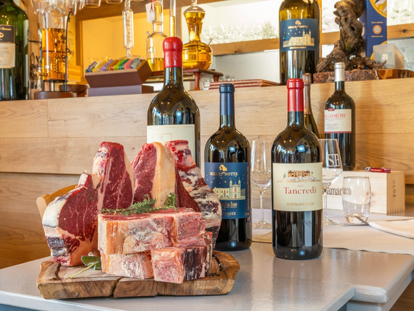 Des steaks crus sur une planche en bois, accompagnés de plusieurs bouteilles de vin, dans un restaurant.