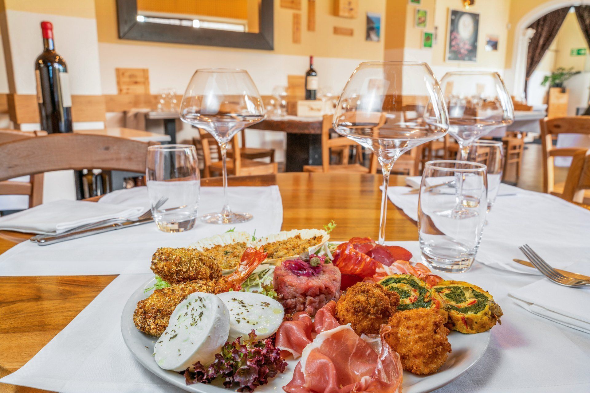 Assiette d'amuse-gueules sur une table dressée pour le dîner, avec des verres à vin et des bouteilles dans un restaurant.