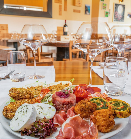 Une assiette blanche garnie de mets variés, des verres à vin et des verres à eau sur une nappe blanche dans un restaurant.