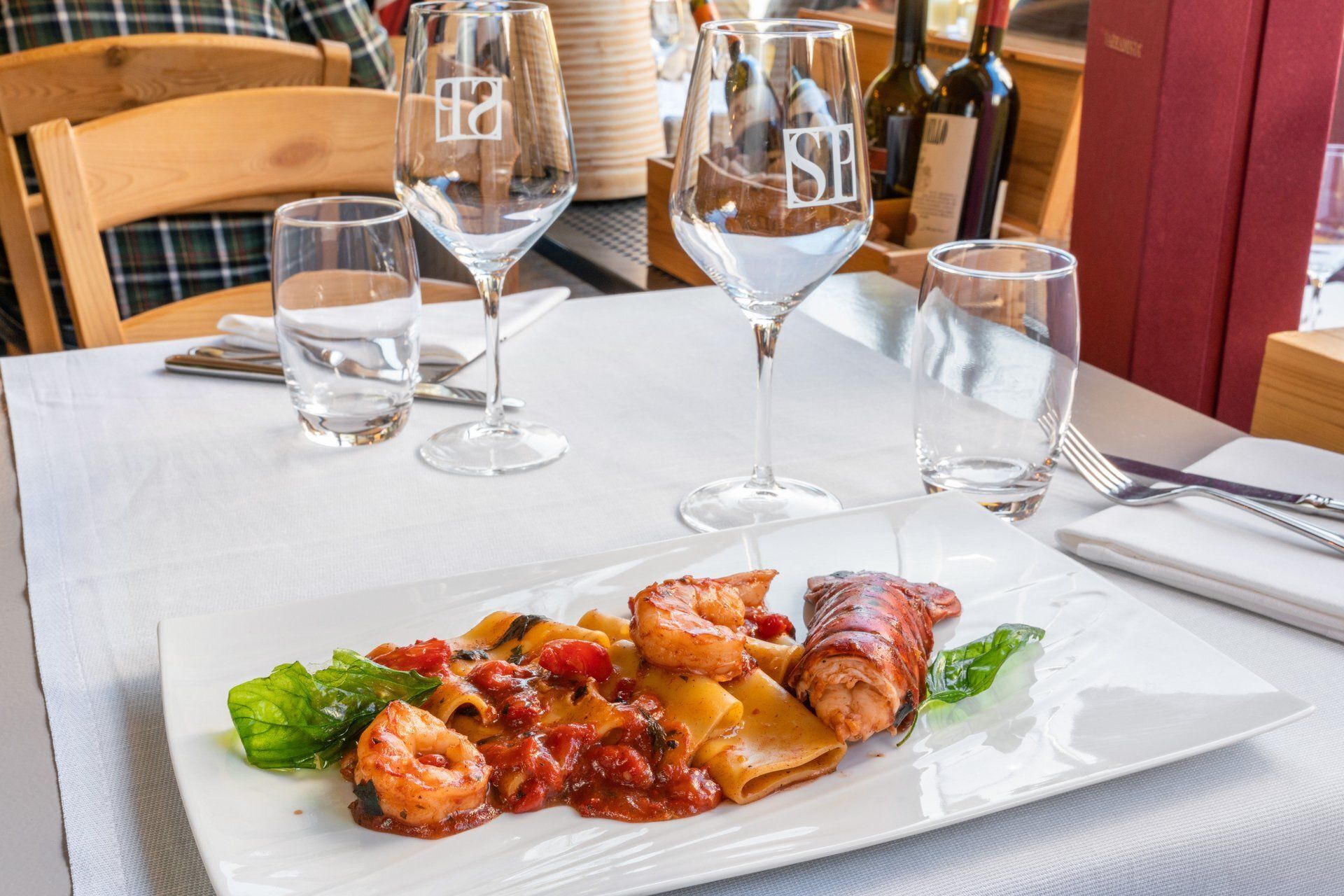 Assiette de pâtes aux crevettes et à la sauce tomate sur une nappe blanche, verres et bouteille de vin.