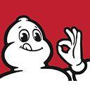 Bonhomme Michelin, silhouette blanche souriante faisant le signe « OK » de la main. Fond rouge.