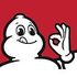 Bonhomme Michelin, silhouette blanche souriante faisant le signe « OK » de la main. Fond rouge.