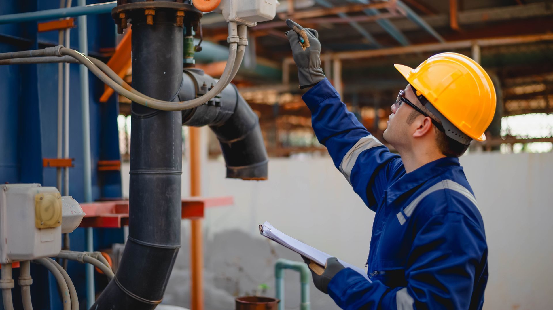 Engineer in yellow hard hat inspecting industrial pipes at a construction site, holding a clipboard. Engineer in yellow hard hat inspecting industrial pipes at a construction site, holding a clipboard.