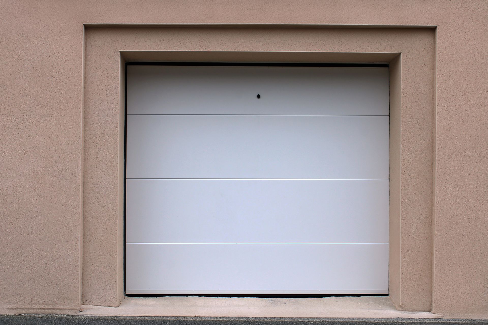 Closed white garage door in a beige stucco wall