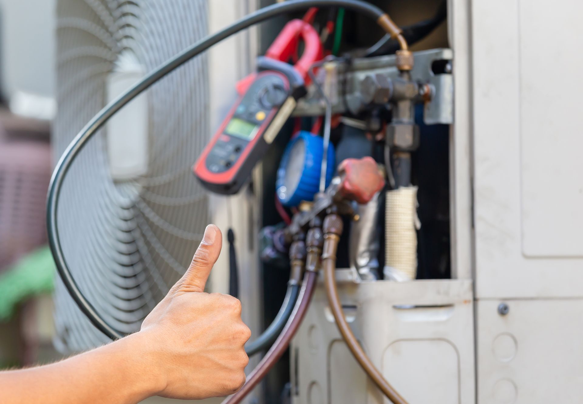 Technician inspecting HVAC unit with manifold gauges while a hand gives a thumbs-up. Technician inspecting HVAC unit with manifold gauges while a hand gives a thumbs-up.