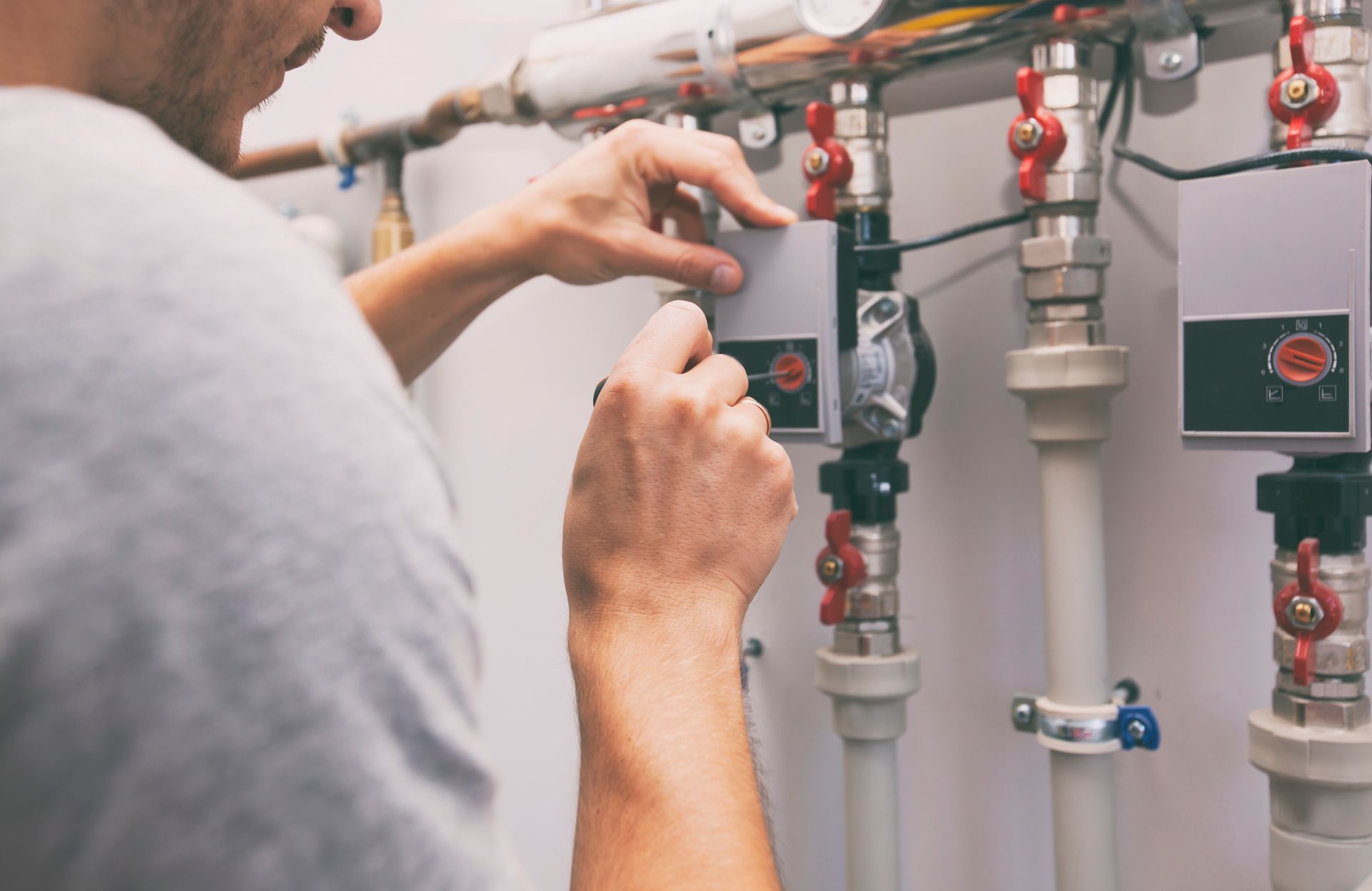 Technician adjusting valves and pipes on industrial plumbing equipment in a utility room