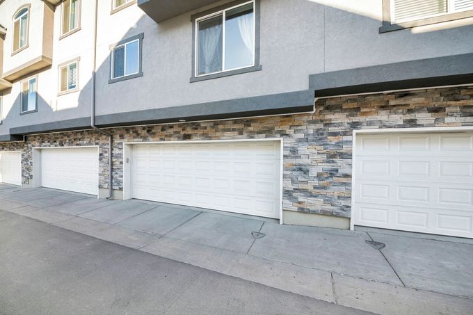 Row of white garage doors on a modern apartment building with stone accents and a sloped driveway