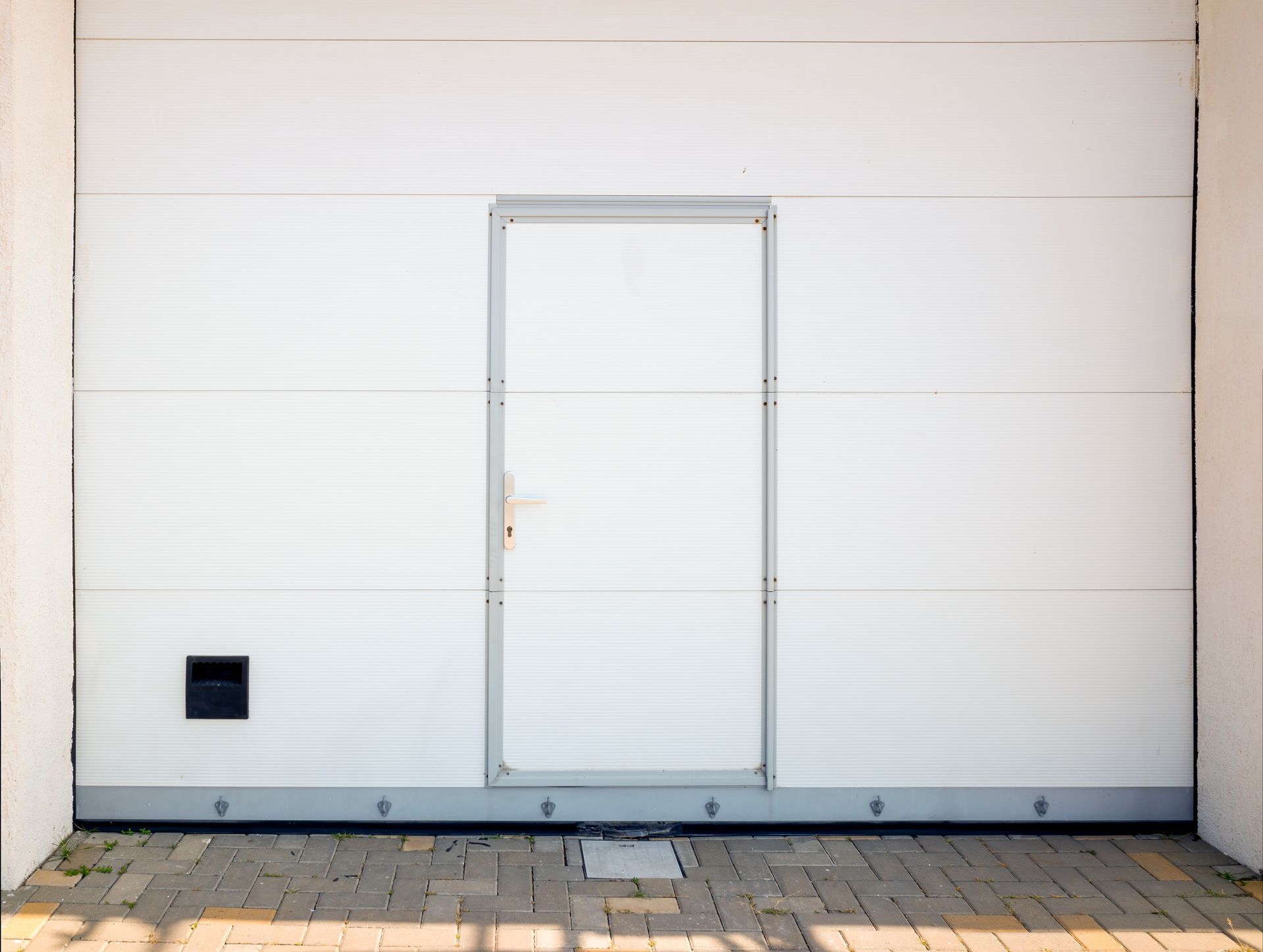 Technician lubricating garage door track hardware on a ladder beside a two-car garage — garage door maintenance in Benton