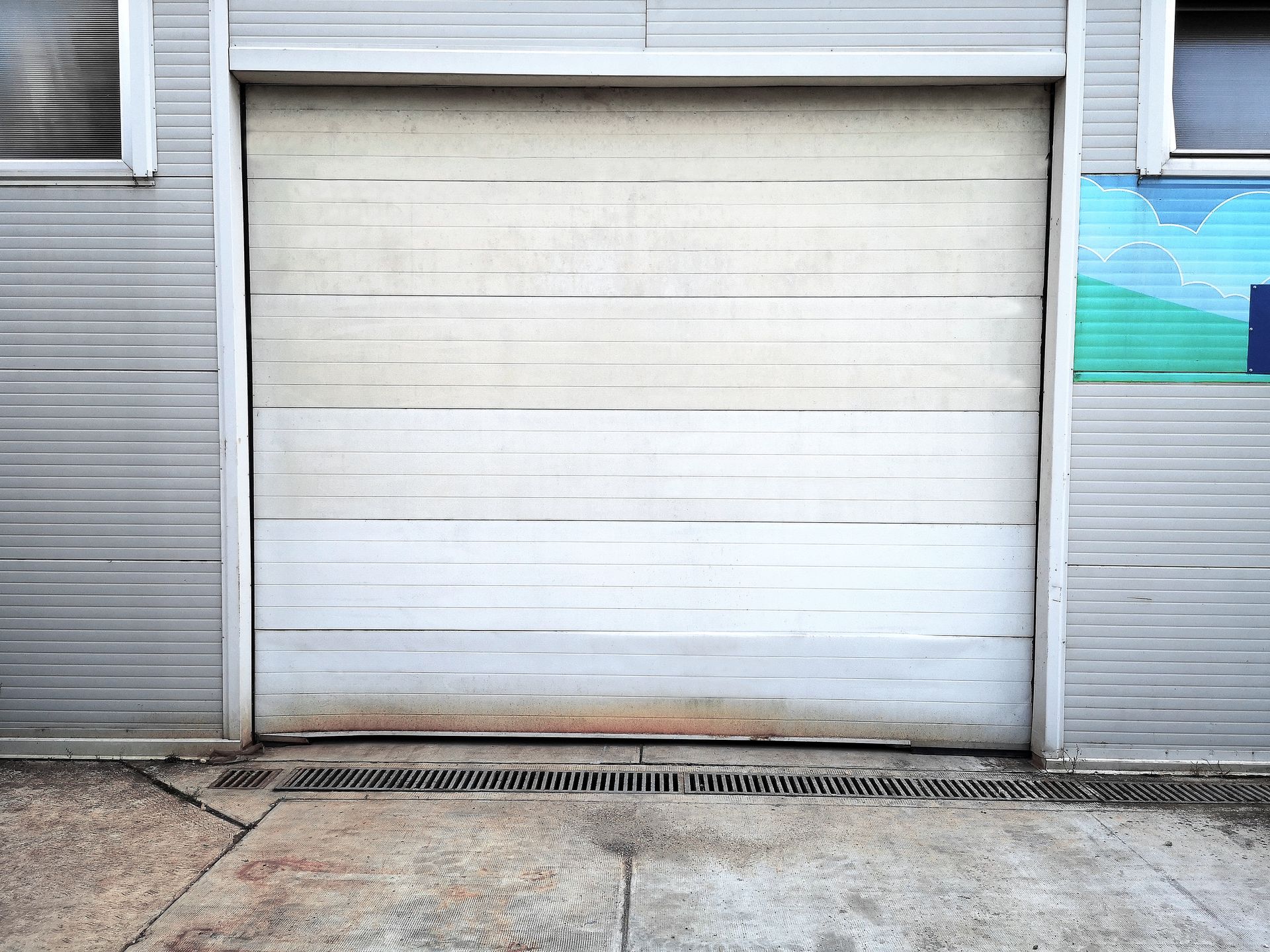 Closed white garage door on a gray building with a concrete sidewalk in front