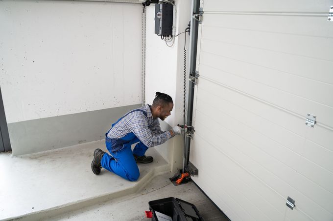 Person kneeling in a garage, adjusting a garage door track with tools nearby.