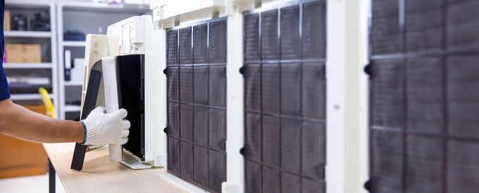 Gloved worker handling a black server component beside a row of computer servers in a lab.