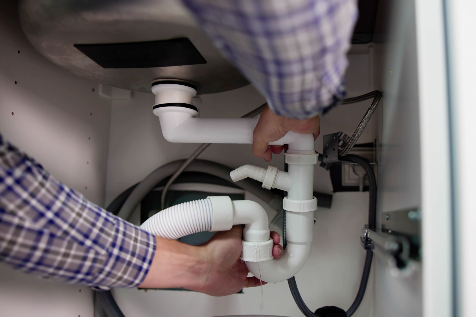 Hands installing white sink drain pipes inside a cabinet under a sink Hands installing white sink drain pipes inside a cabinet under a sink