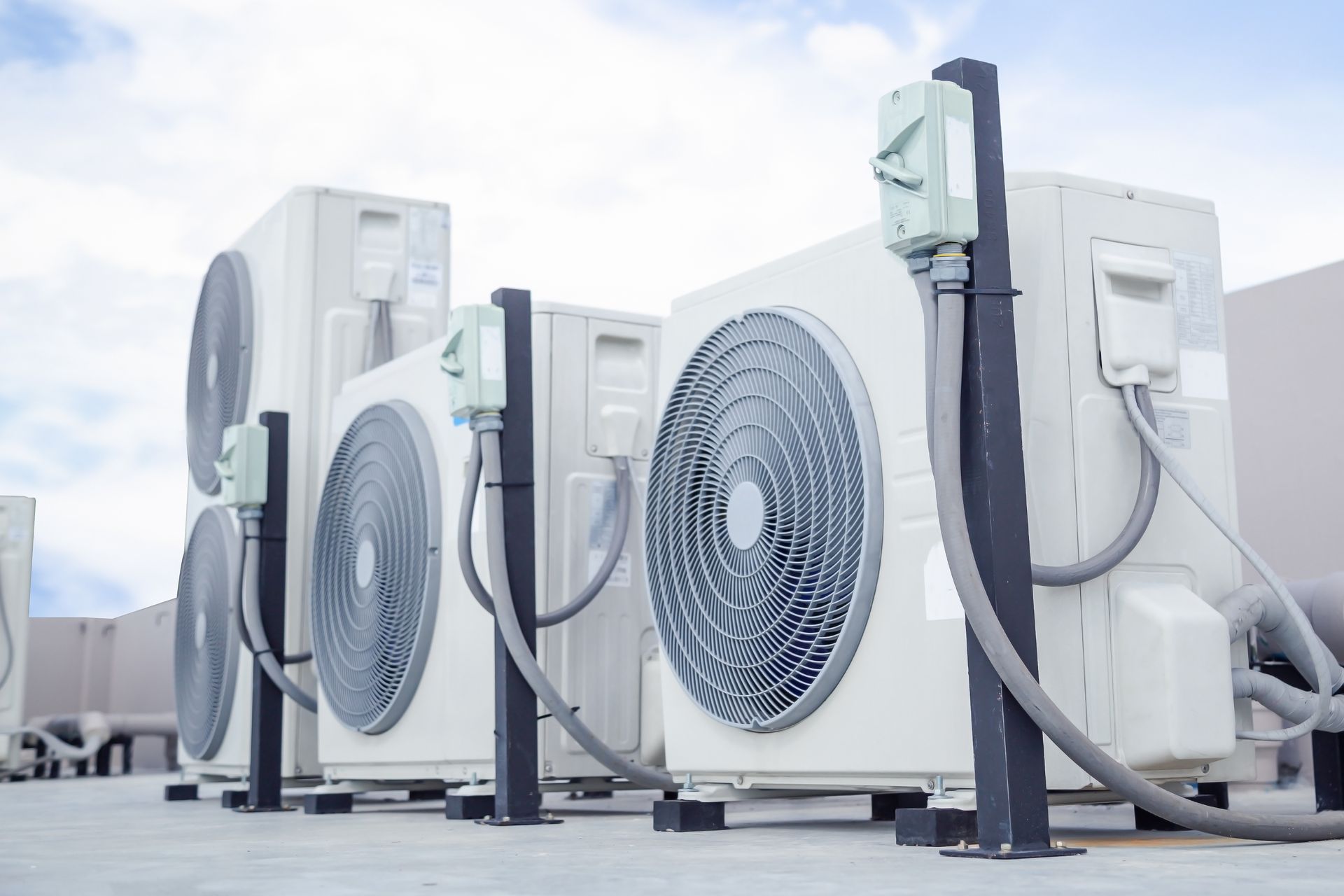 Outdoor HVAC condensers lined up on a rooftop, with large circular fans and piping. Outdoor HVAC condensers lined up on a rooftop, with large circular fans and piping.
