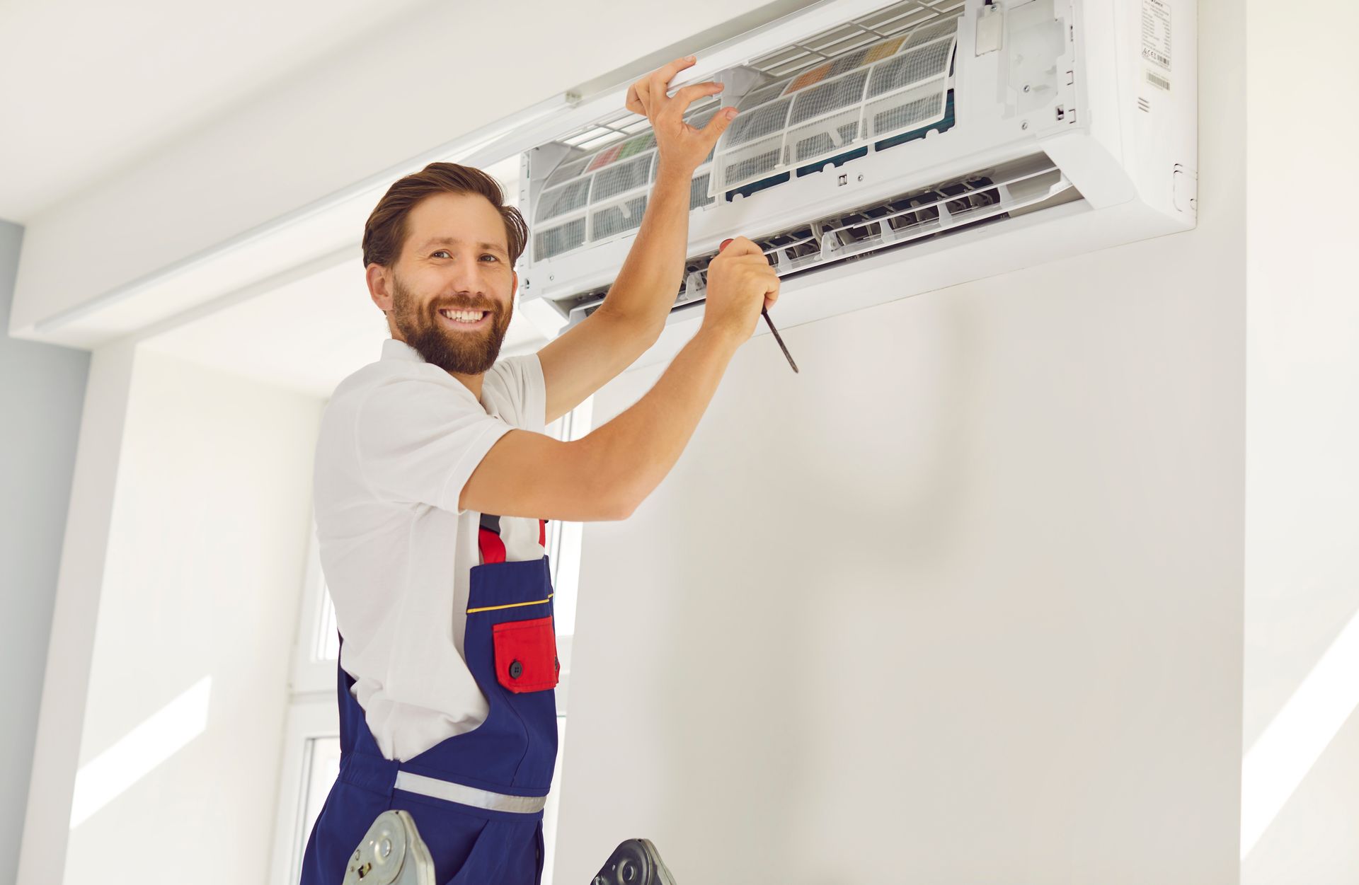 Technician servicing a wall-mounted air conditioner with tools in a bright room