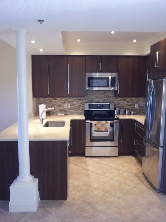 Modern kitchen with dark brown cabinets, stainless steel appliances, and beige countertops.