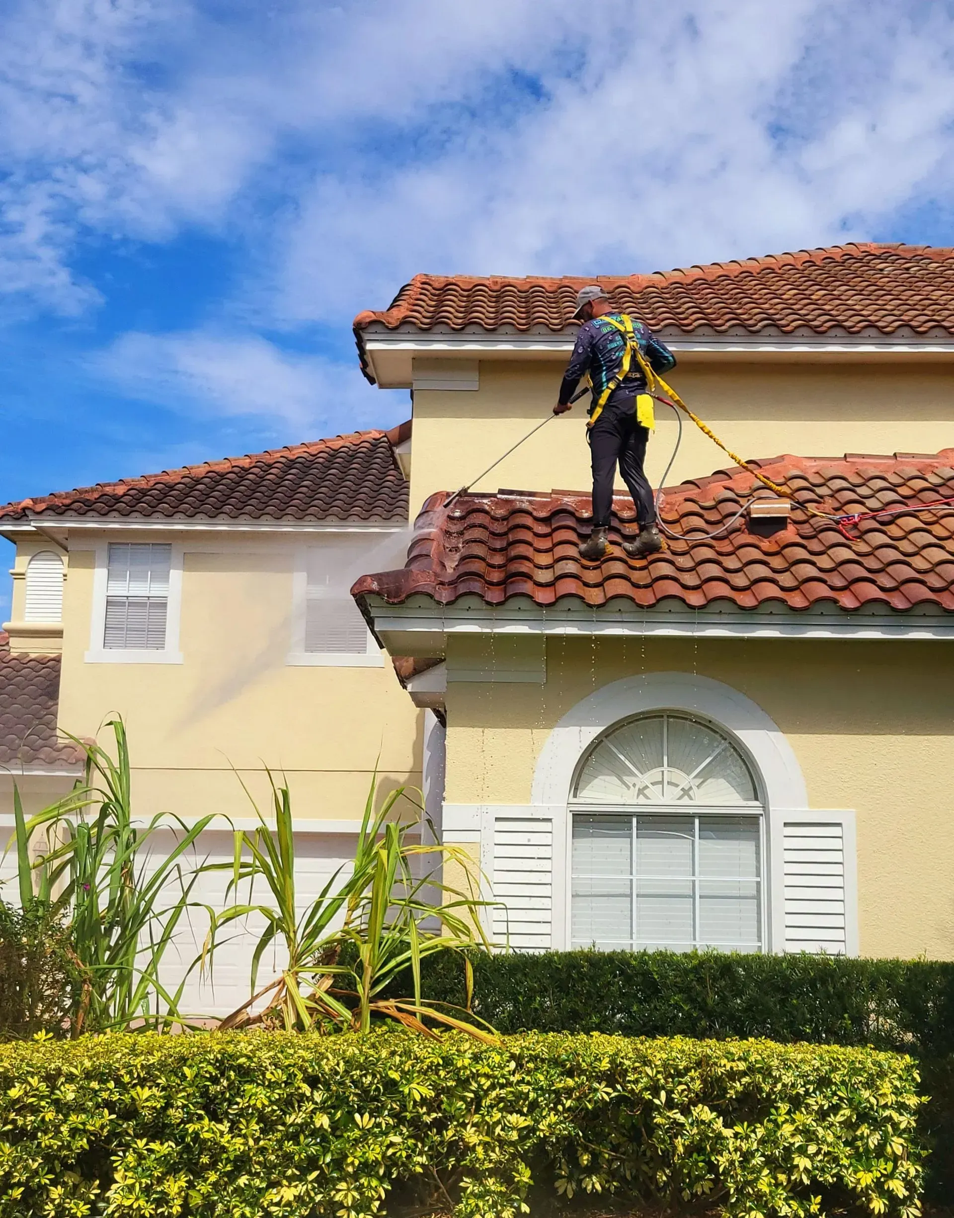 Worker in safety gear repairing a red-tiled roof on a cream-colored house