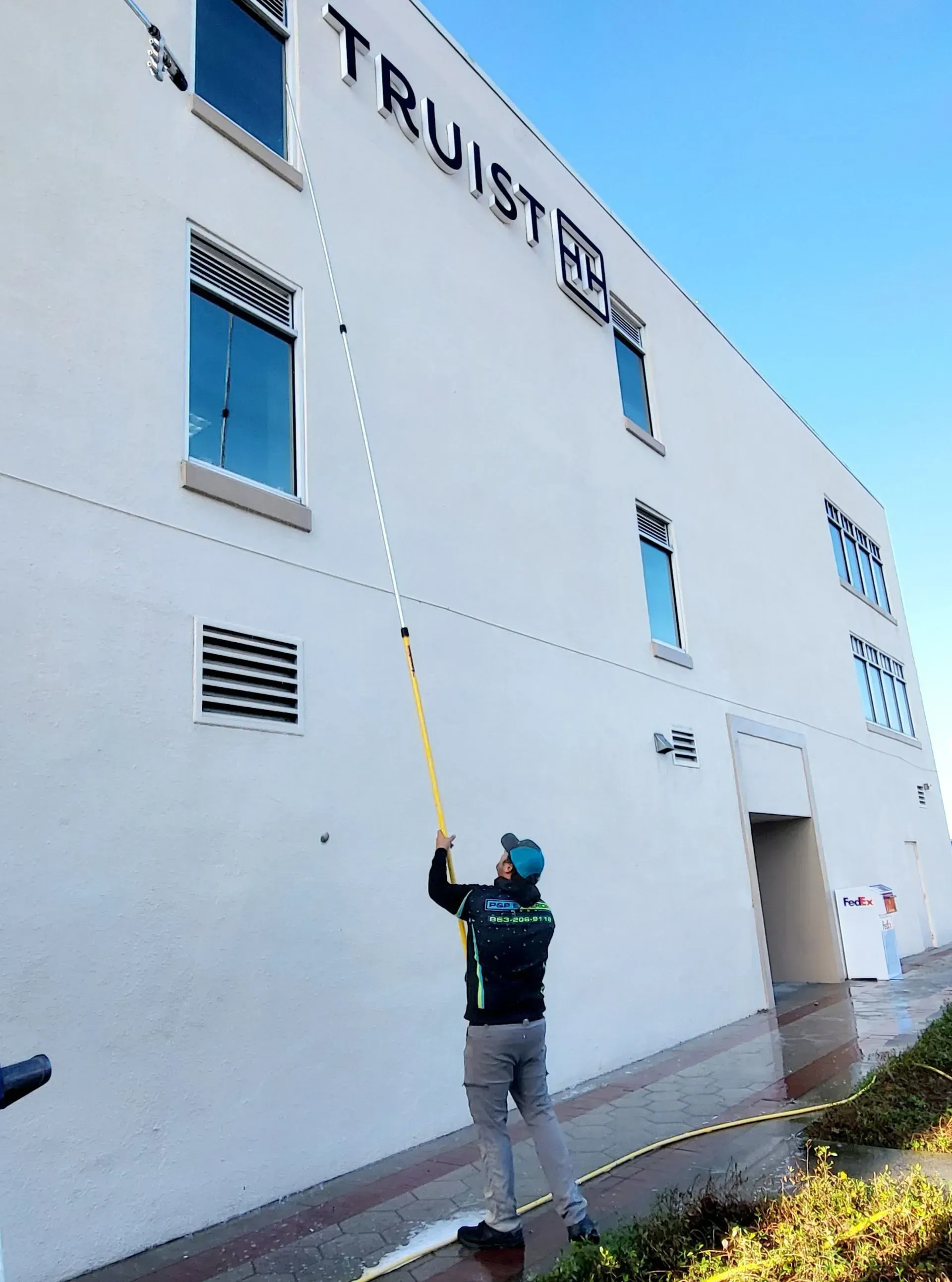 Worker on a rope cleaning a white building exterior with blue sky above.