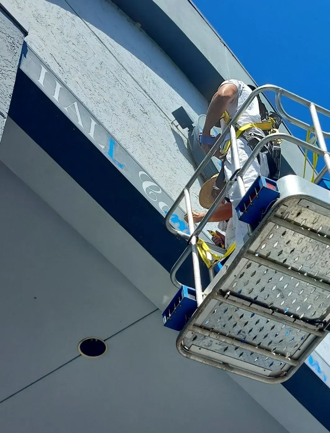 Worker on a raised platform painting the side of a building against a blue sky