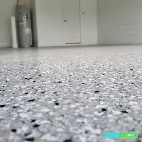Low-angle view of a speckled gray floor in a room with white cabinets and a silver canister in the corner
